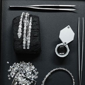 Serpenti Viper gold and diamond bracelets, loose diamonds, magnifying glass and pliers on a black tray.