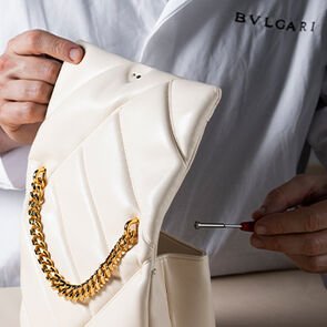 Craftsman fixing a chain handle on the Serpenti Cabochon bag in white quilted calf leather, close up.