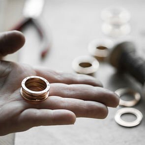 Craftsman holding a completed B.zero1 ring with single parts of the ring in the background, close-up.