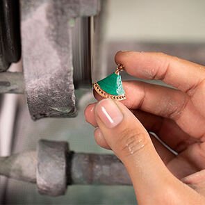 Craftswoman holding a rose gold Divas’ Dream element with malachite insert during manufacture, close-up.