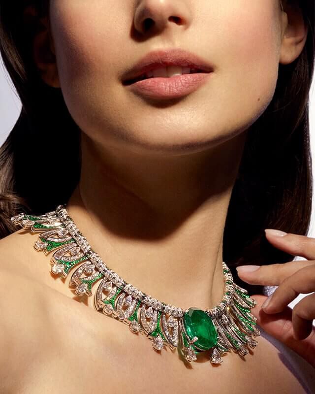 Model wearing the Eden High Jewellery platinum necklace with emeralds and diamonds, close up.