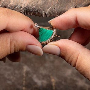 Craftswoman setting a malachite insert into a rose gold Divas’ Dream pendant during manufacture, close-up.