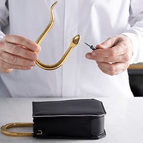 Artisan attaching the metallic snake-shaped handle to the Serpentine Vertical tote in black calf leather. Artisan attaching the metallic snake-shaped handle to the Serpentine Vertical tote in black calf leather.