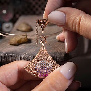 Craftswoman assembling the Divas' Dream rose gold pendant with diamonds and pink sapphires, close up.