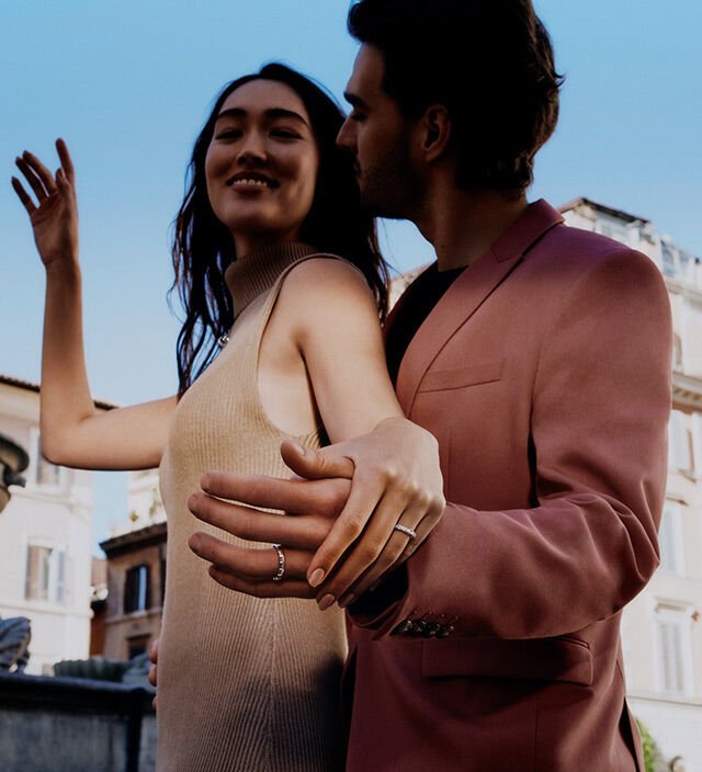 Man embracing his beloved from behind while wearing Bulgari wedding bands, Roman backdrop. Man embracing his beloved from behind while wearing Bulgari wedding bands, Roman backdrop.