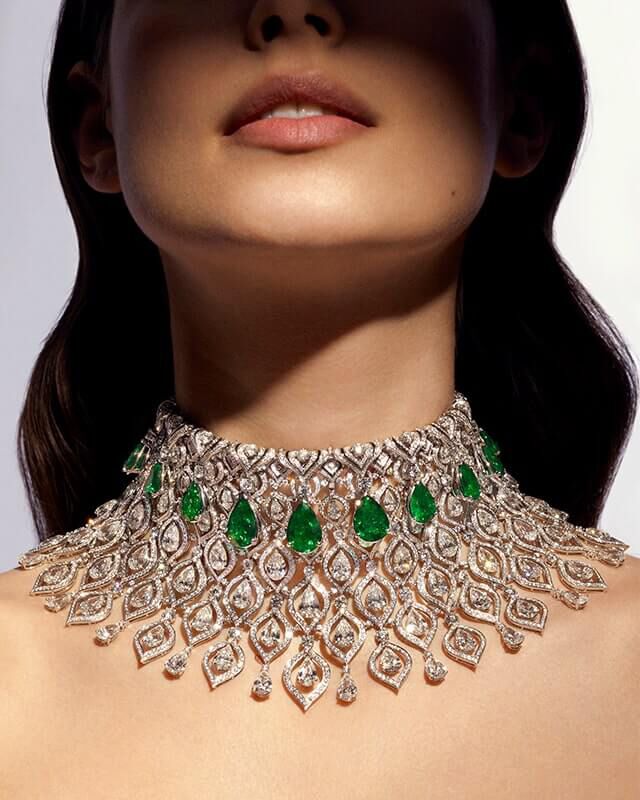 Model wearing the Eden High Jewellery platinum necklace with emeralds and diamonds, close up.