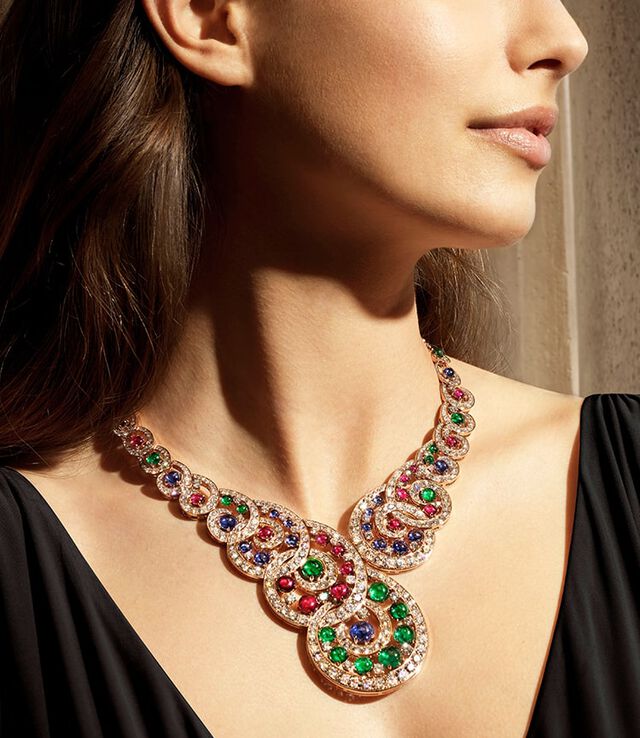 Model wearing a Magnifica High Jewelry rose gold necklace with cabochon emeralds, rubies and sapphires, and diamonds.