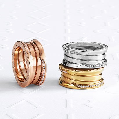 B.zero1 rings in rose, white and yellow gold with demi pavé diamonds on the edges, against a logo backdrop.