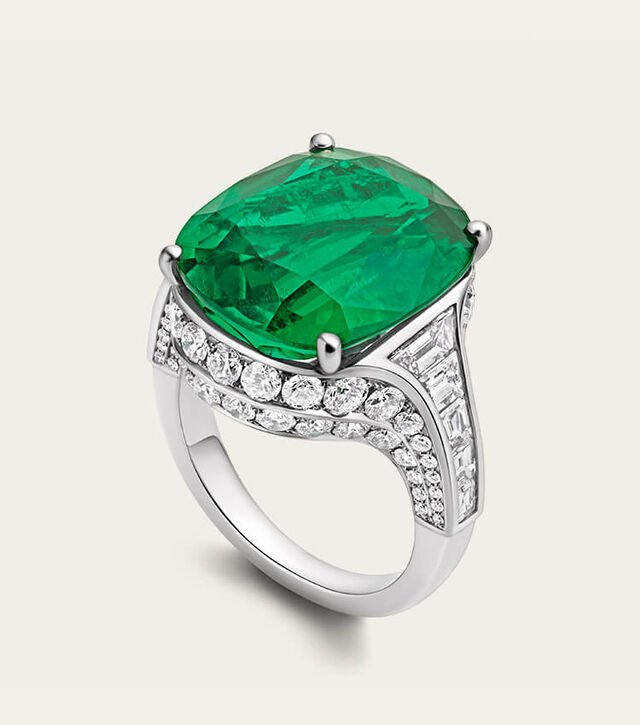 Eden High Jewellery Ring aus Platin mit einem Smaragd und Diamanten, Nahaufnahme vor einem Hintergrund mit Bulgari Logo. Eden High Jewellery Ring aus Platin mit einem Smaragd und Diamanten, Nahaufnahme vor einem Hintergrund mit Bulgari Logo.